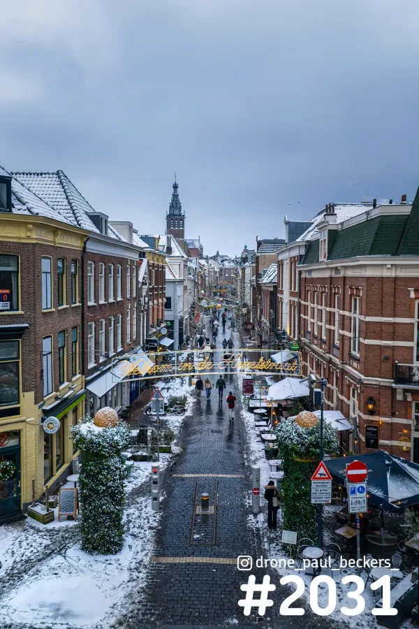 Besneeuwde straat in het centrum van Nijmegen met Stevenskerktoren aan het eind en gouden lichtslinger boven de straat