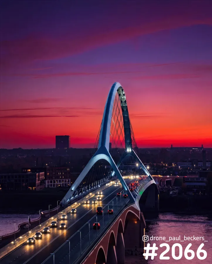 Luchtfoto van De Oversteek in Nijmegen in de avondschemering, met verkeer op de brug en een rood-paarse lucht