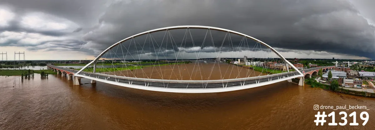 Panorama van brug De Oversteek over de bruine Waal bij Nijmegen-Lent, met een donkere onweerslucht boven de stad