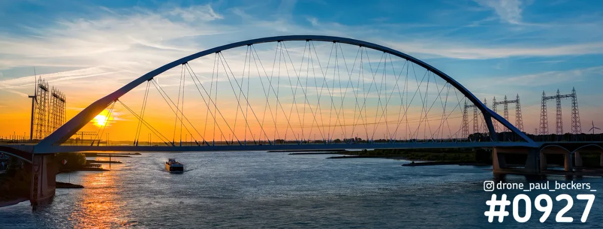 Panorama van brug De Oversteek over de Waal bij Nijmegen met zonsondergang, een binnenvaartschip en hoogspanningsmasten
