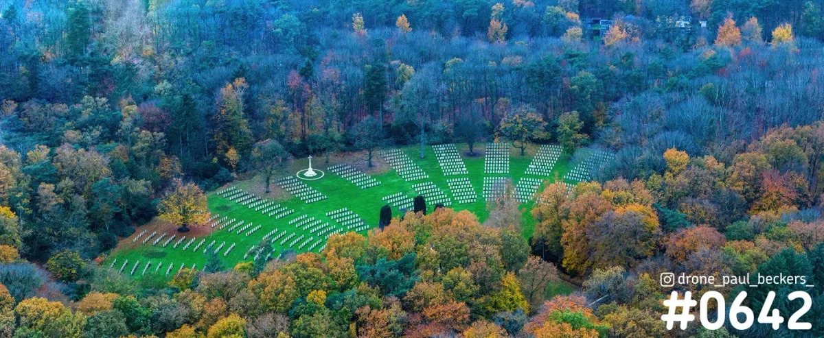Luchtfoto van een begraafplaats met rijen witte grafstenen op een grasveld in herfstbos bij de Goffert in Nijmegen