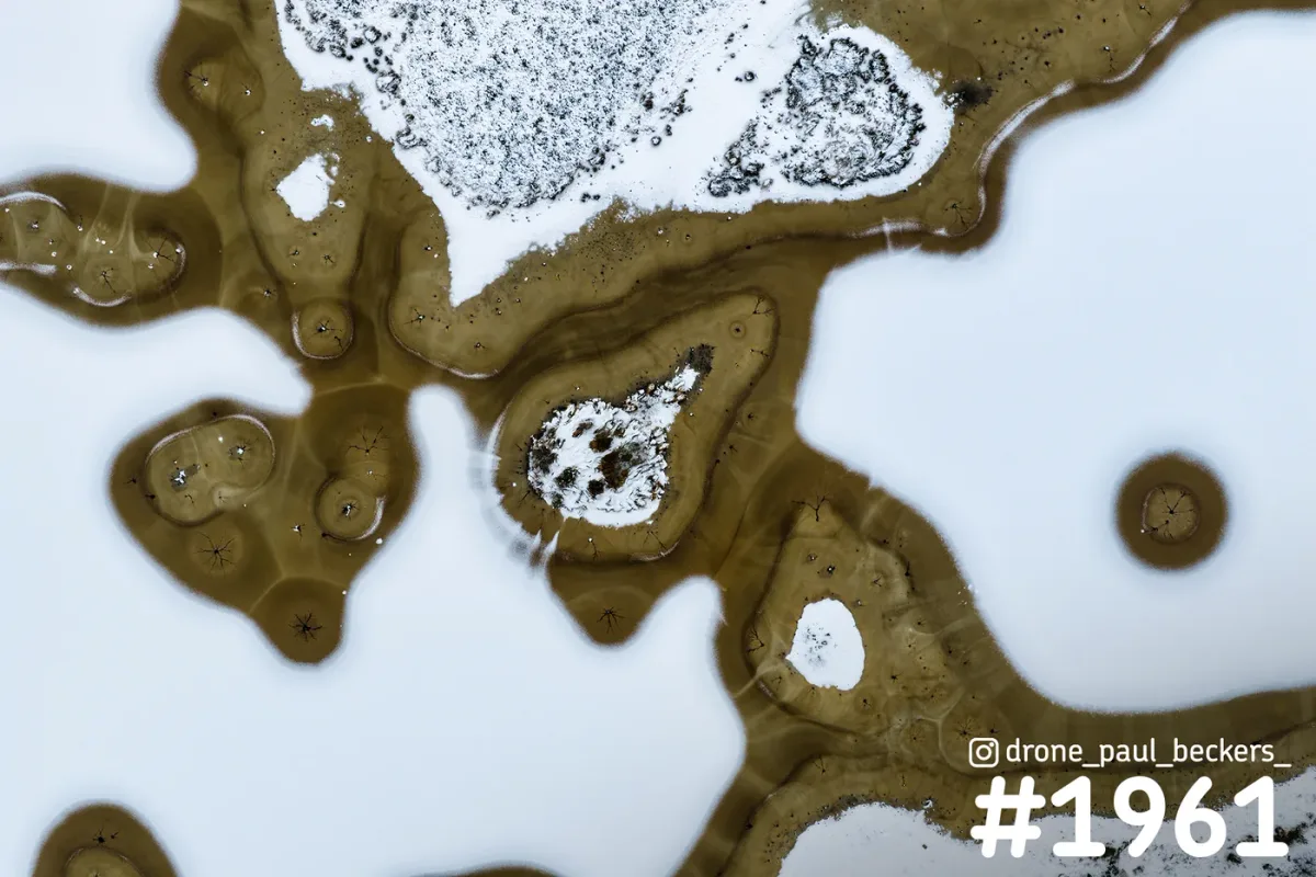 Luchtfoto van de Hatertse Vennen met sneeuw en ijs: witte vlakken tussen bruin water en rietkragen, van recht boven gezien