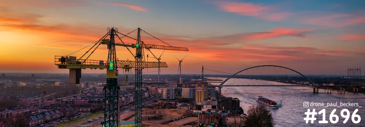 Luchtfoto van Nijmegen bij zonsondergang met bouwkranen in het Havenkwartier, de boogbrug De Oversteek en een schip op de Waal