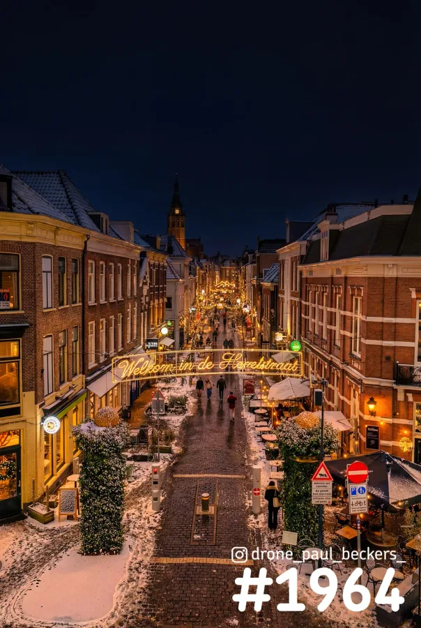 Luchtfoto van de besneeuwde Hemelstraat in Nijmegen in de avond, met verlicht welkomstbord en de Stevenskerktoren