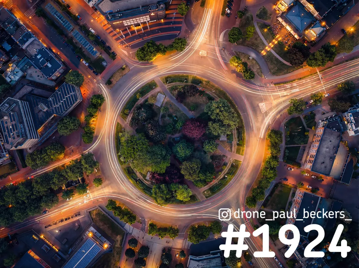 Luchtfoto van het Keizer Karel Plein in Nijmegen in de avondschemering, met lichtsporen van verkeer rond het groene midden