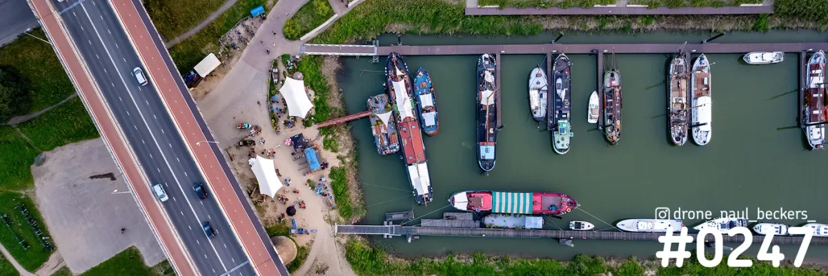 Luchtfoto recht van boven op de Lindenberghaven in Nijmegen met afgemeerde schepen en een weg met rood fietspad