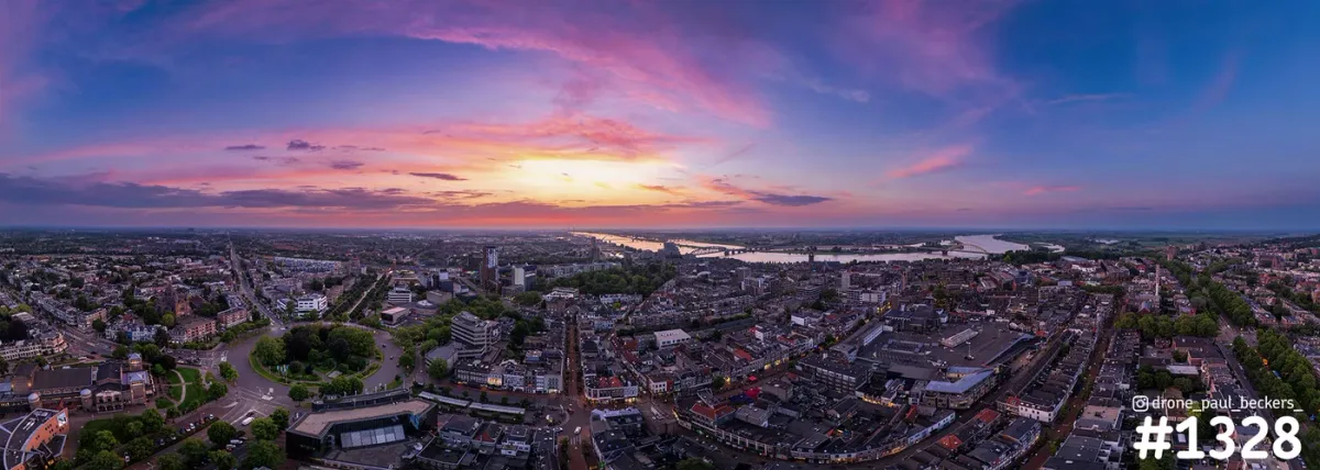 Panoramische luchtfoto van het centrum van Nijmegen bij zonsondergang, met paarsroze lucht en de Waal aan de horizon