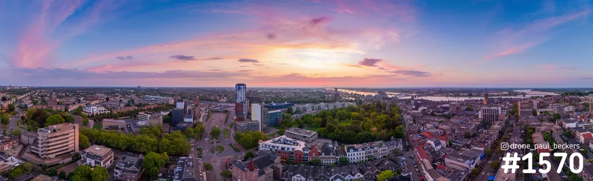 Panoramafoto van Nijmegen in de schemering met roze wolken boven het centrum, Kronenburgerpark en de Waal