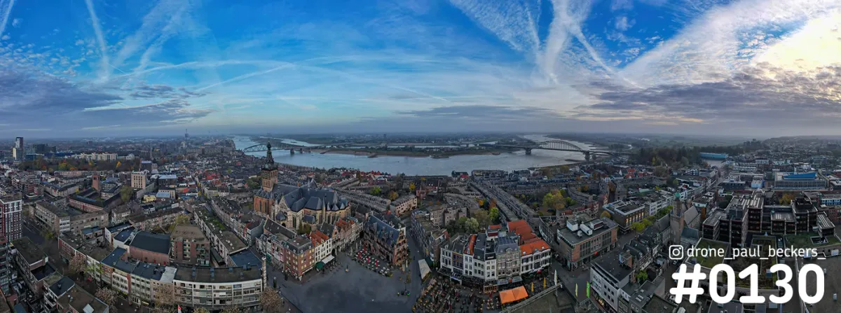 Panoramische luchtfoto van Nijmegen met Stevenskerk, de Waal en twee bruggen onder een blauwe lucht met sluierwolken