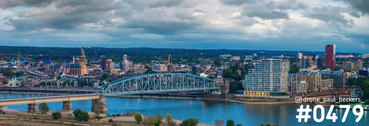Panorama van Nijmegen met boogbrug over de Waal, Stevenskerk links en Nimbus aan de Handelskade rechts onder wolken