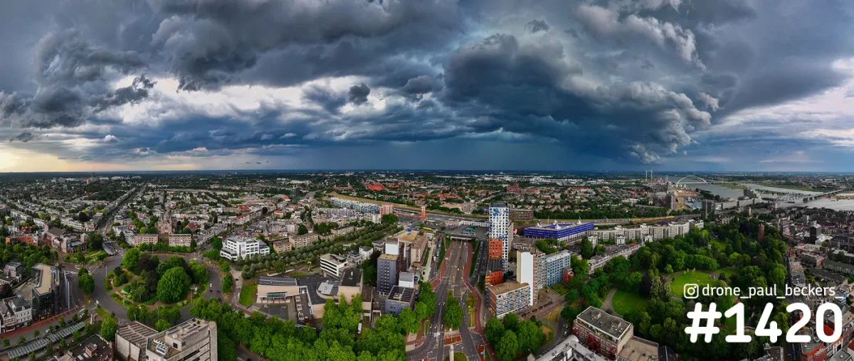 Luchtfoto van Nijmegen met donkere onweerswolken boven het Stationsgebied, de Waal en De Oversteek aan de horizon