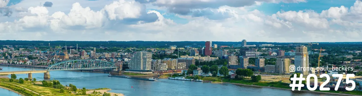 Luchtfoto panorama van Nijmegen aan de Waal met een stalen boogbrug en woontorens van de Handelskade onder stapelwolken