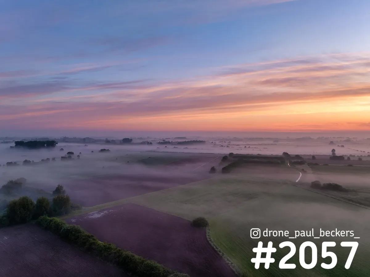 Luchtfoto van de Ooijpolder bij Nijmegen vlak voor zonsopkomst, met mist tussen akkers en bomenrijen onder een roze en oranje lucht