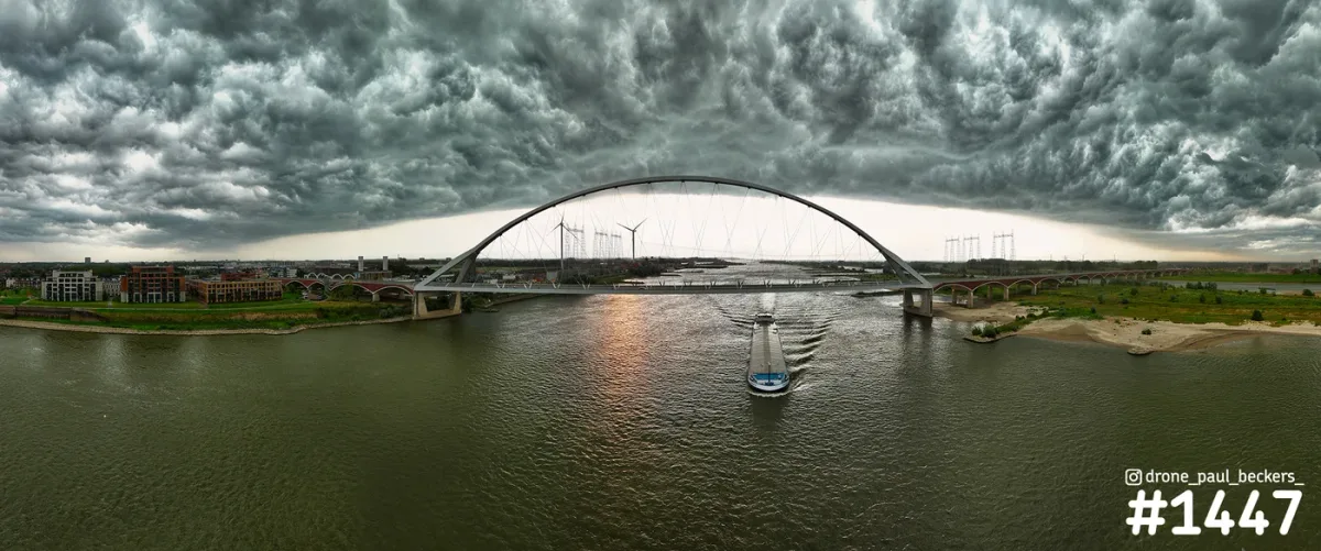 Luchtfoto van De Oversteek over de Waal in Nijmegen met dreigende wolken en een schip onder de brugboog