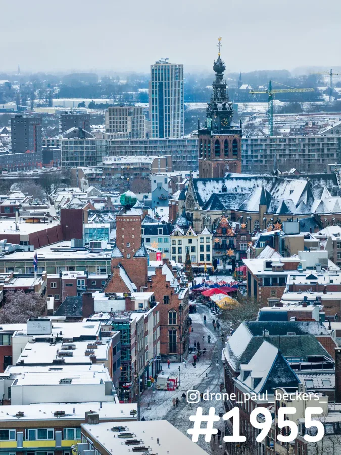 Luchtfoto van de besneeuwde daken van het centrum van Nijmegen met de Stevenskerk en kraampjes op de Grote Markt