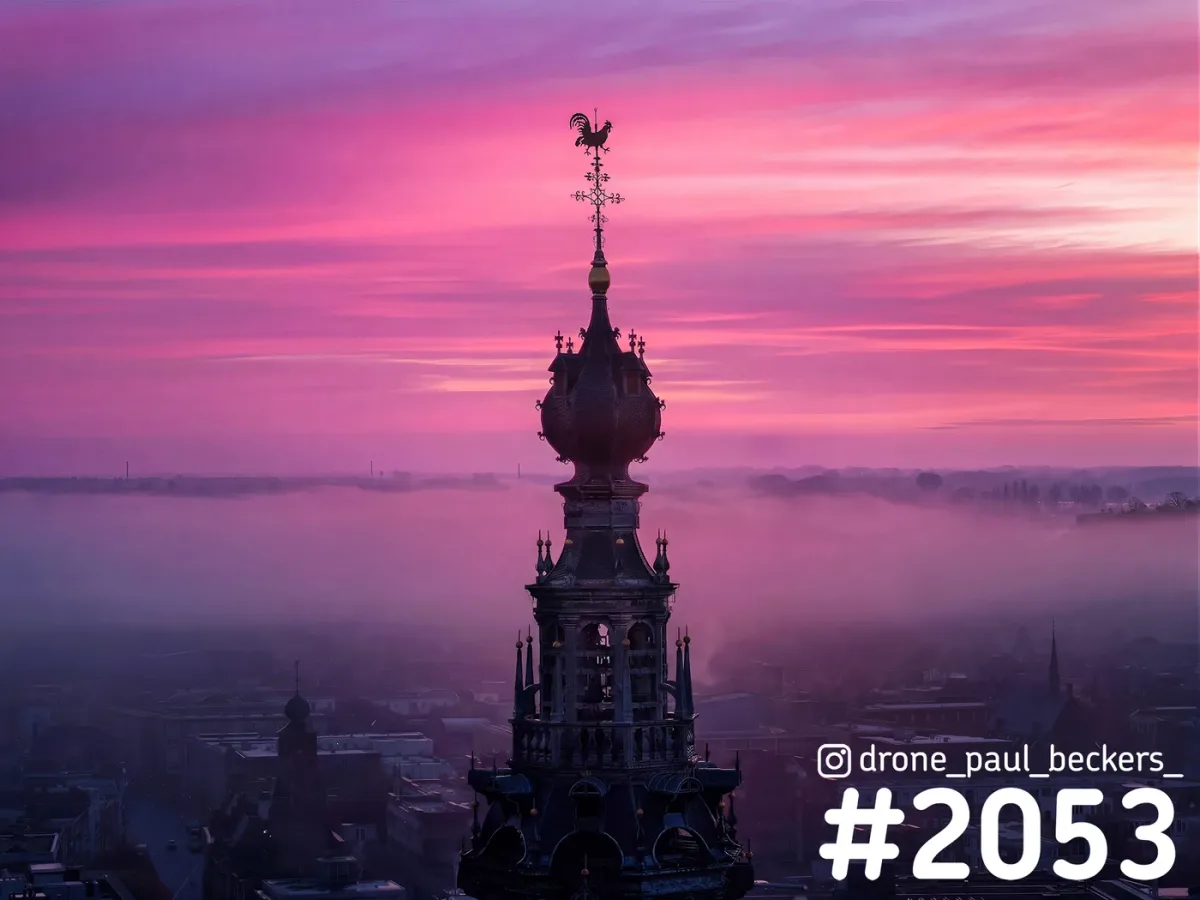 Luchtfoto van de toren van de Stevenskerk in Nijmegen met roze ochtendlucht en mist boven de daken van het centrum