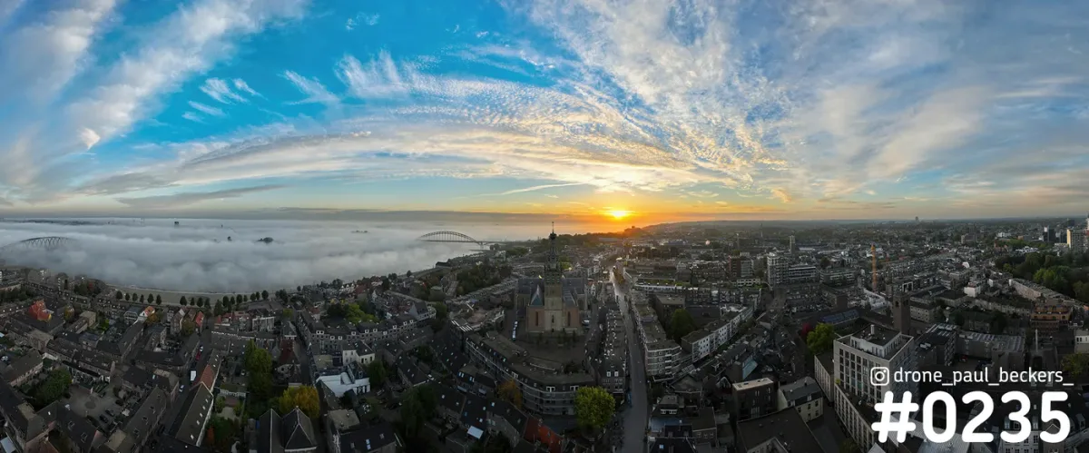 Panorama van Nijmegen van boven bij zonsopkomst, met de Stevenskerk in het centrum en mist boven de Waal bij de Waalbrug