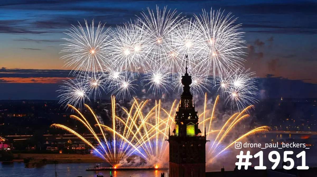 Luchtfoto van vuurwerk boven de Waal in Nijmegen, met de verlichte toren van de Stevenskerk in de avondschemering