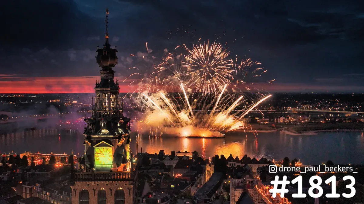 Luchtfoto van vuurwerk boven de Waal in Nijmegen met de verlichte Stevenskerktoren en een rode avondgloed