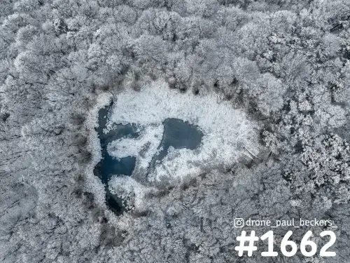 Luchtfoto van een bevroren poel op de Duivelsberg bij Nijmegen, omringd door bomen met rijp en wit bevroren oevers