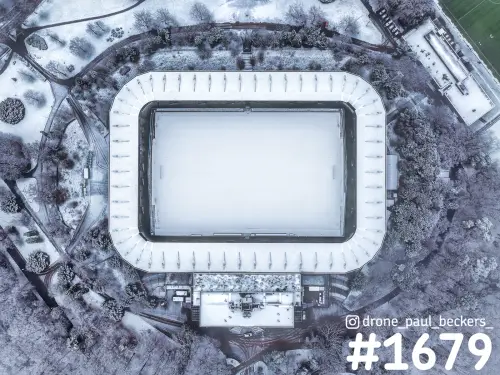 Luchtfoto recht van boven van een stadion bij de Goffert in Nijmegen, met sneeuw op het veld, het dak en de bomen