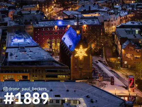 Luchtfoto van de Marienburg kapel in Nijmegen, blauw verlicht dak en lichtgevende sneeuwvlok, daken met sneeuw bij avond