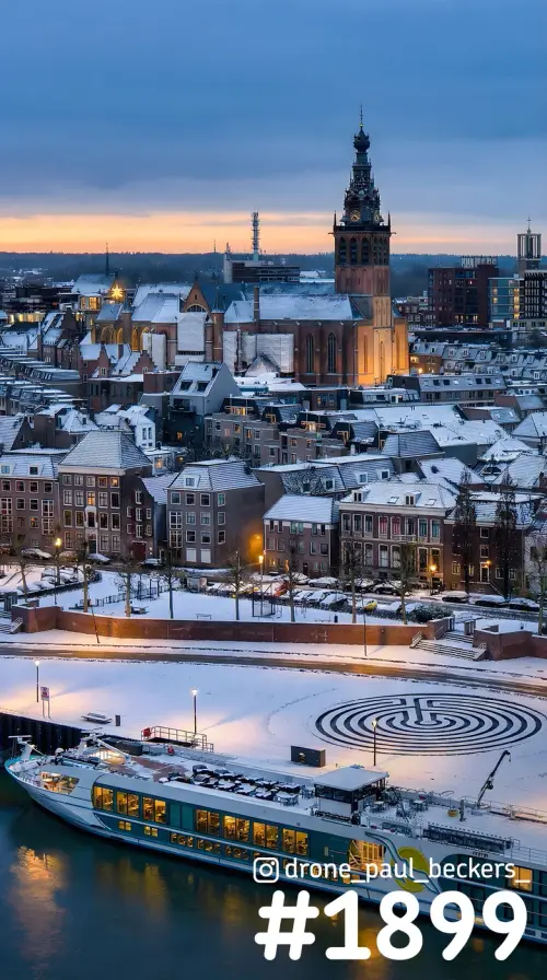 Besneeuwd centrum van Nijmegen met Stevenskerk in de schemering, rivierschip aan de Waal en een cirkelpatroon in de sneeuw