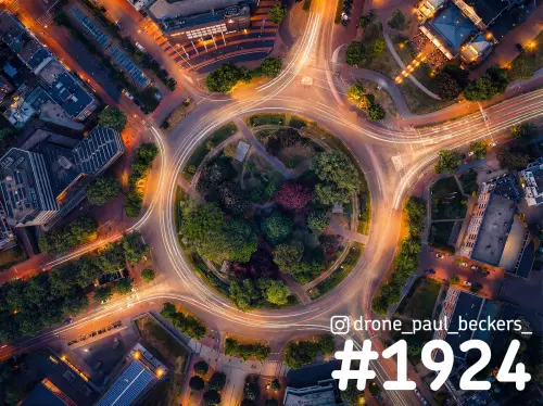Luchtfoto van het Keizer Karel Plein in Nijmegen in de avondschemering, met lichtsporen van verkeer rond het groene midden