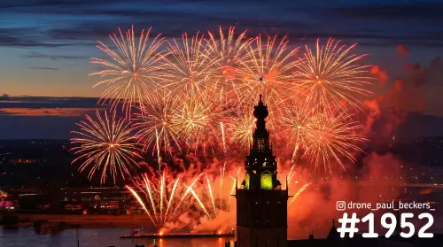 Luchtfoto van vuurwerk achter de toren van de Stevenskerk in Nijmegen, met rode rook en een ponton op de Waal
