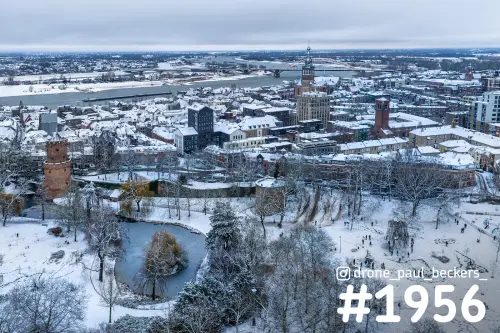 Luchtfoto van het besneeuwde centrum van Nijmegen met de Stevenskerk, de Waal en de Waalbrug onder een grijze winterlucht