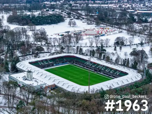 Luchtfoto van voetbalstadion bij de Goffert in Nijmegen in de sneeuw, met groen grasveld en rood-witte circustenten