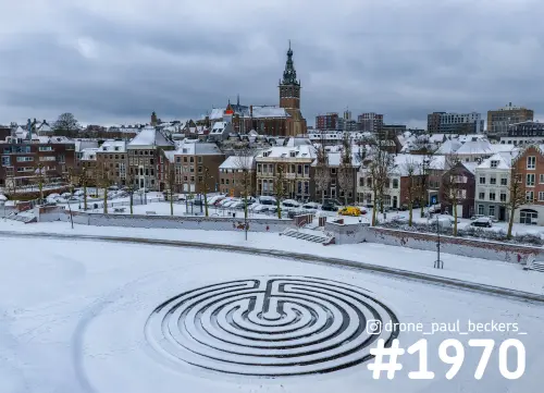 Luchtfoto van een labyrint in de sneeuw op de Waalkade in Nijmegen, met de Stevenskerk boven besneeuwde daken