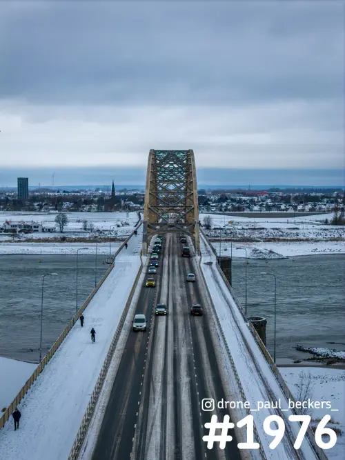 Luchtfoto van de Waalbrug in Nijmegen in de sneeuw, met verkeer op de brug en een fietser op het besneeuwde fietspad