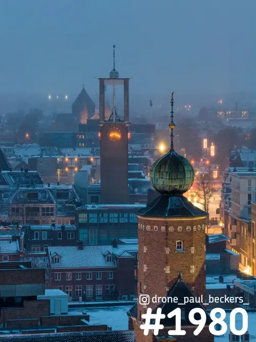 Luchtfoto van het centrum van Nijmegen in de avondmist, met sneeuw op de daken en een bakstenen toren met groene koepel