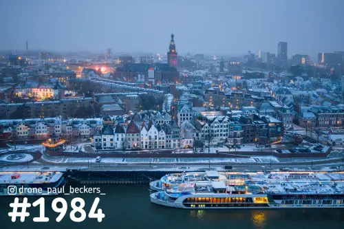 Luchtfoto van de Waalkade in Nijmegen in de schemering, met sneeuw op de daken en rivierschepen aan de kade