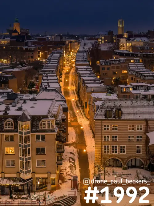 Luchtfoto van een besneeuwde straat bij de Waalkade in Nijmegen in de avond, met oranje straatlicht en sneeuw op de daken
