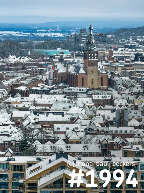 Luchtfoto van de Stevenskerk in Nijmegen tussen besneeuwde daken, met kale bomen van het Kronenburgerpark