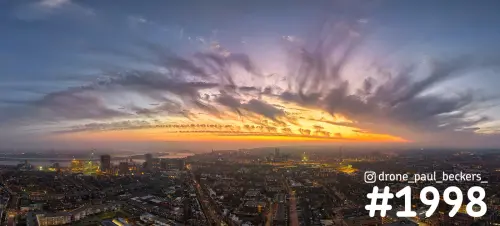 Luchtfoto van Nijmegen in de schemering, met een oranje gloed aan de horizon en uitwaaierende wolkenstrepen boven de stad