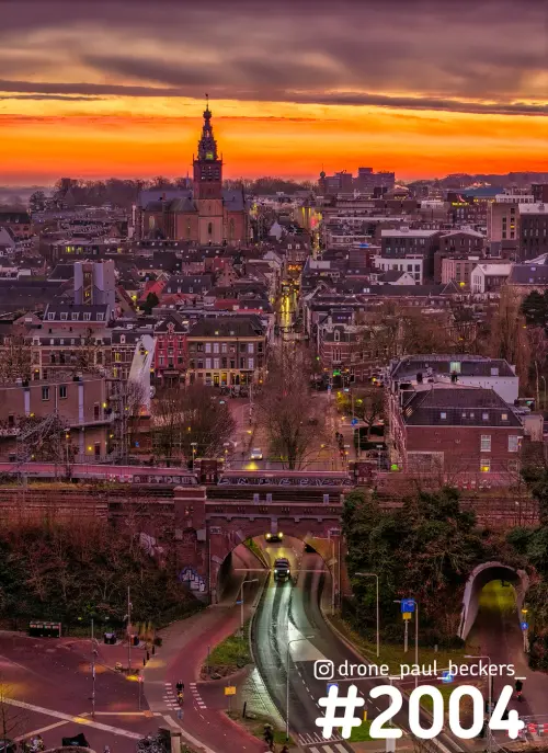 Luchtfoto van de Stevenskerk in Nijmegen bij zonsondergang, met spoorviaduct en verlichte weg op de voorgrond