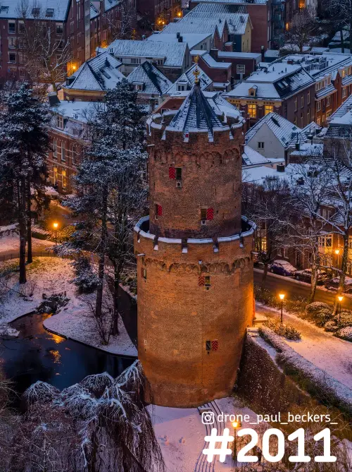 Luchtfoto van een ronde bakstenen toren in het Kronenburgerpark in Nijmegen, schemer met sneeuw op daken en bomen