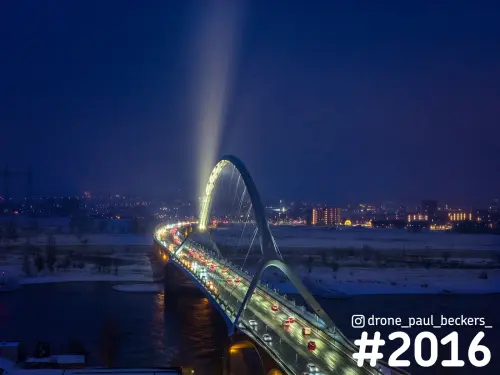 Luchtfoto van brug De Oversteek in Nijmegen in de avond, met een lichtbundel boven de boog en sneeuw langs de Waal