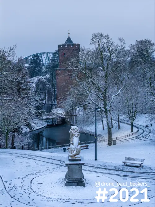 Kronenburgerpark in Nijmegen onder sneeuw, met stenen leeuw, rode baksteentoren en besneeuwde bomen langs de vijver