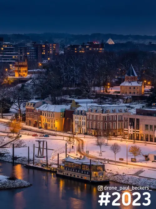 Luchtfoto van de Waal en het Valkhofgebied in Nijmegen na zonsondergang, sneeuw op de kade en een boot aan het water