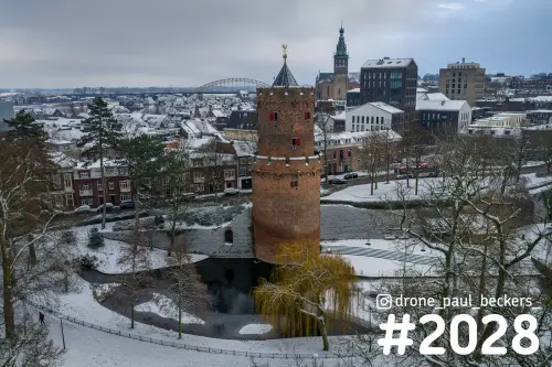 Luchtfoto van een bakstenen toren in het Kronenburgerpark in Nijmegen, met sneeuw en de Stevenskerk op de achtergrond