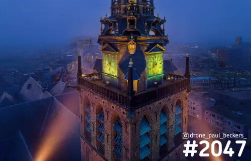 Luchtfoto van de Stevenskerk in Nijmegen in het blauwe uur, met verlichte groene wijzerplaten en mist boven de daken