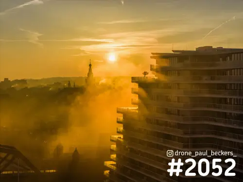 Luchtfoto van een woontoren aan de Handelskade in Nijmegen bij zonsopkomst, met gouden mist rond de Stevenskerk