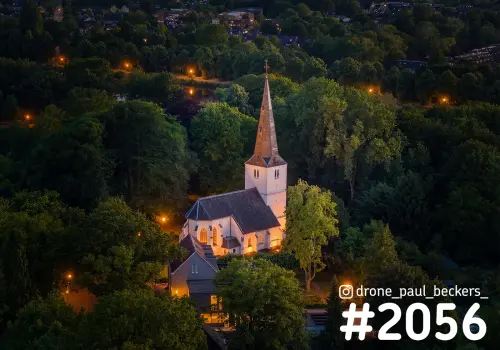 Luchtfoto van een verlicht wit kerkje met spitse toren tussen het groen in Neerbosch-Oost, Nijmegen, in het avondlicht