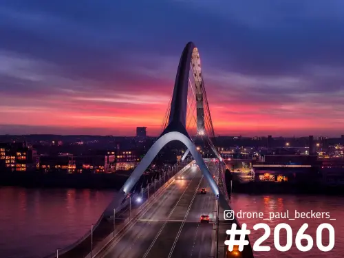Luchtfoto van een boogbrug over de Waal in Nijmegen in de schemering, met roze en paarse lucht boven de rivier