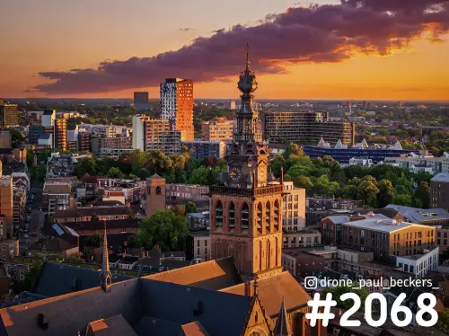 Luchtfoto van de Stevenskerk in Nijmegen bij zonsondergang, met de toren voor daken en hoogbouw en een paarse wolk