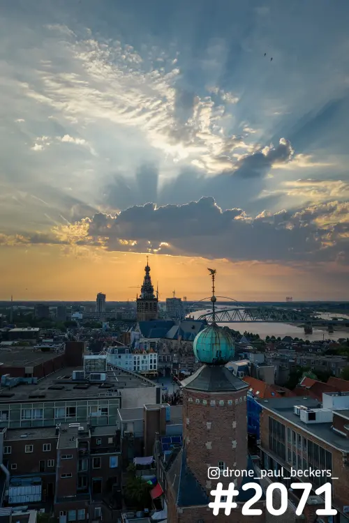 Nijmegen van boven bij zonsondergang: zonnestralen boven Stevenskerk, De Oversteek en een toren met groene koepel